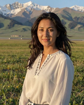 Beautiful Kyrgyz woman in modern blouse with traditional embroidery in alpine meadow setting